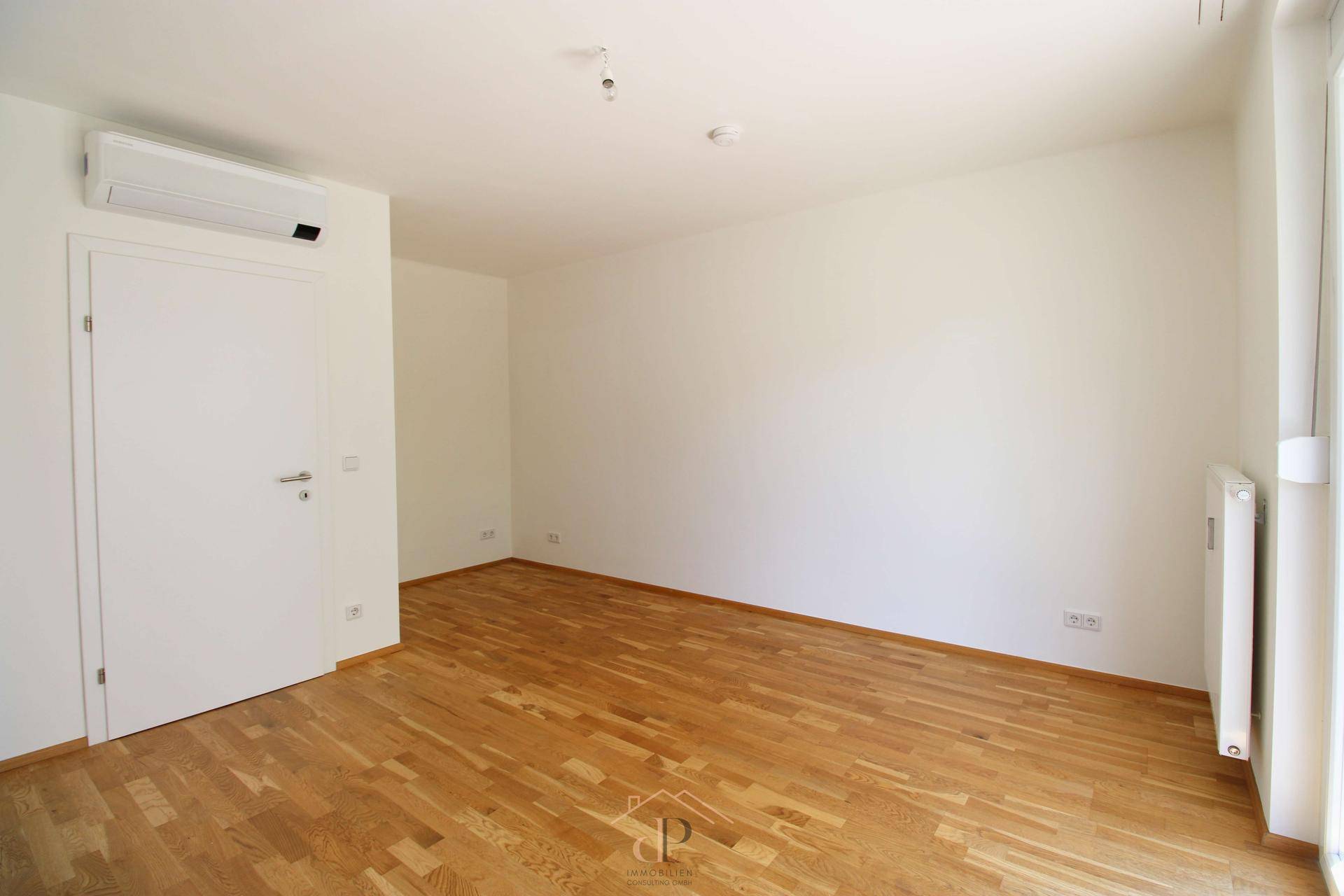Helles Schlafzimmer mit Holzboden, weiß gestrichenen Wänden und Klimaanlage.