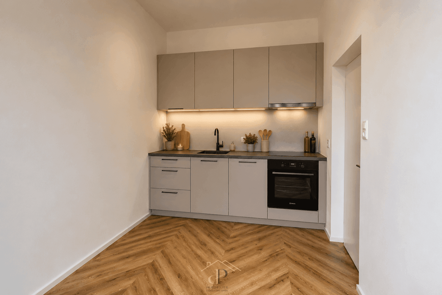 Moderne Küchenzeile mit grauen Schränken, integriertem Backofen und Fischgrätparkettboden.