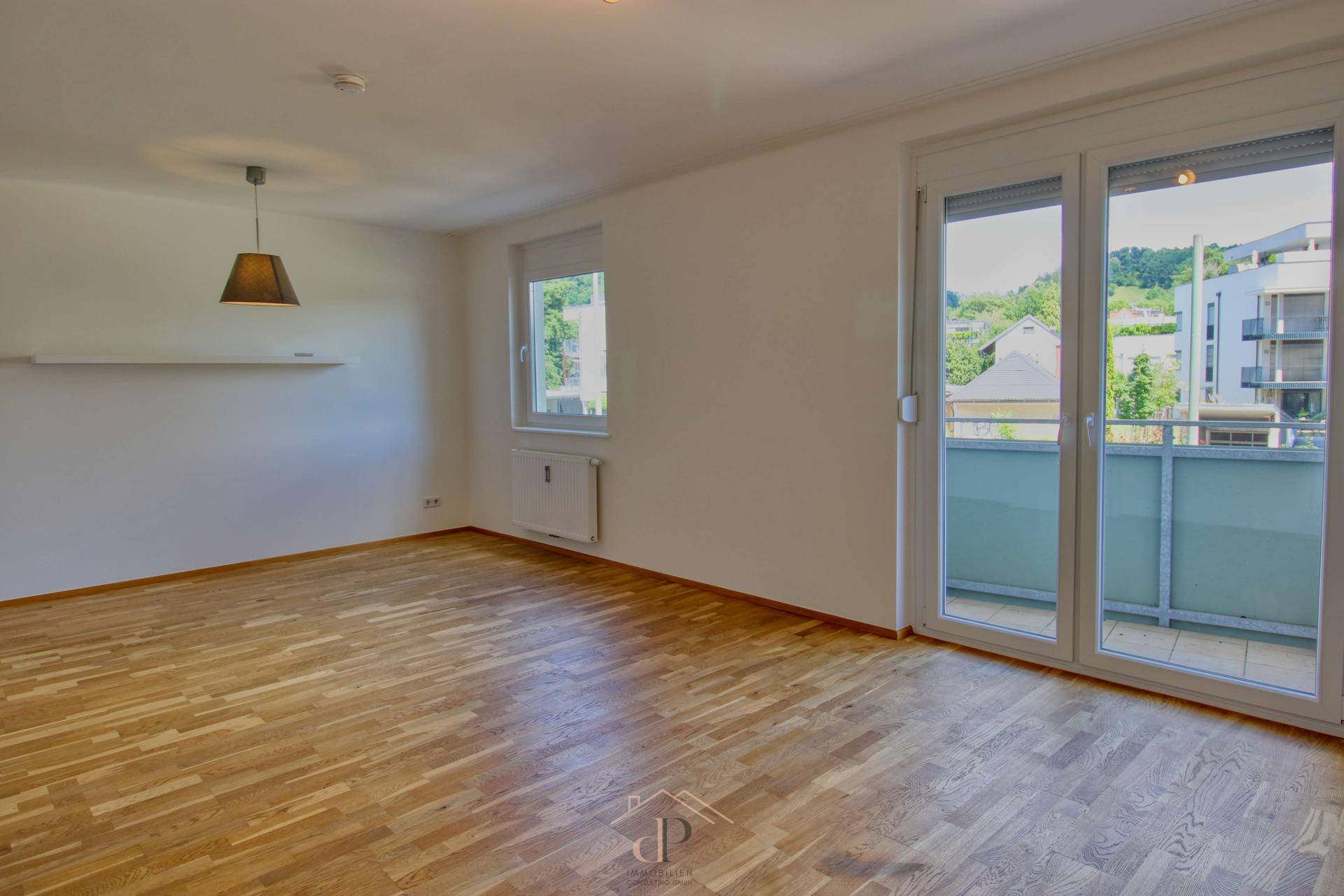 Helles Wohnzimmer mit Holzboden und großem Fenster, bietet Zugang zum Balkon.