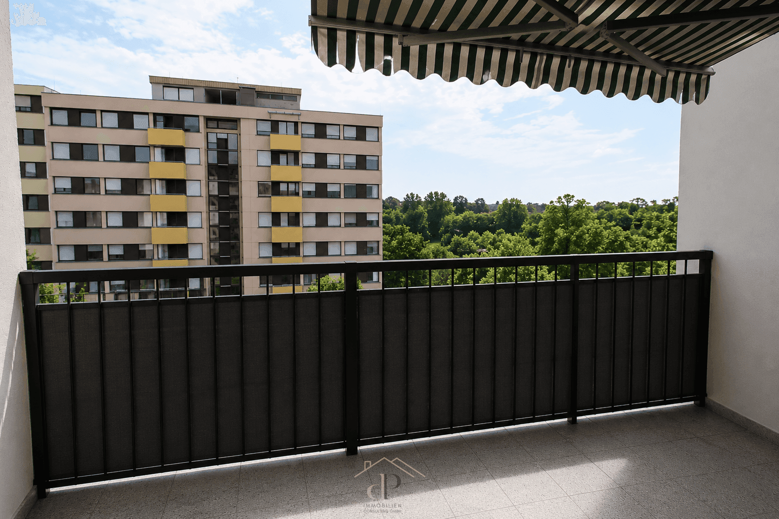 Balkon mit Markise und Blick auf ein Wohngebäude sowie grüne Bäume.