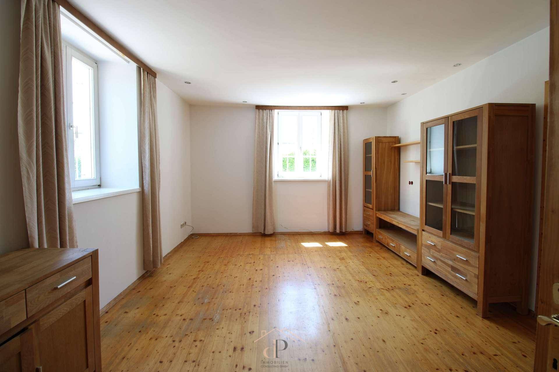 Helles Zimmer mit Holzboden und großen Fenstern, ausgestattet mit Holzmöbeln, bietet viel Tageslicht.