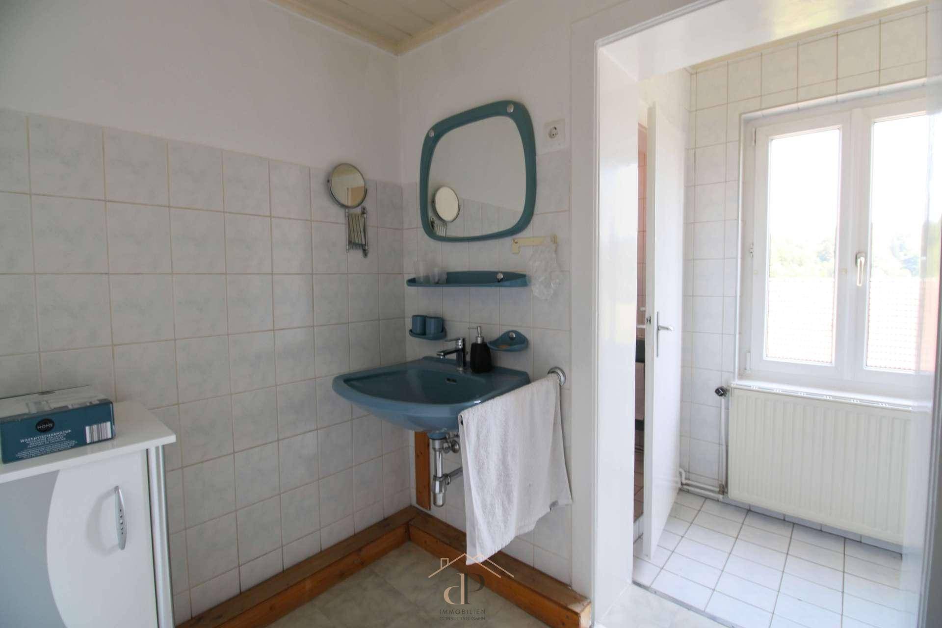 Badezimmer mit hellblauen Fliesen, Waschtisch und Fenster, funktional und gut beleuchtet.
