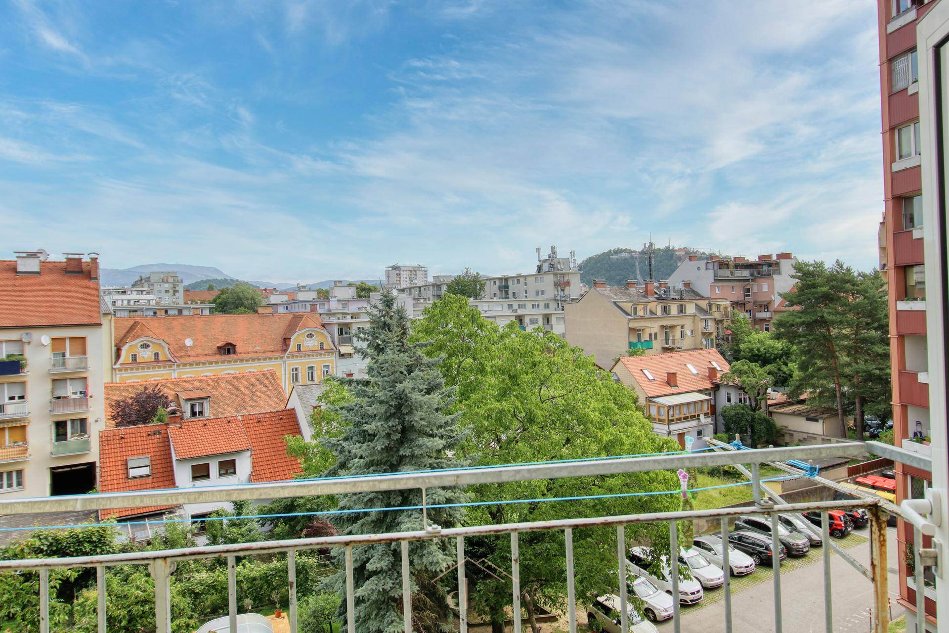 Balkon mit weitem Blick über die Stadt, grüne Bäume und entfernte Hügel.