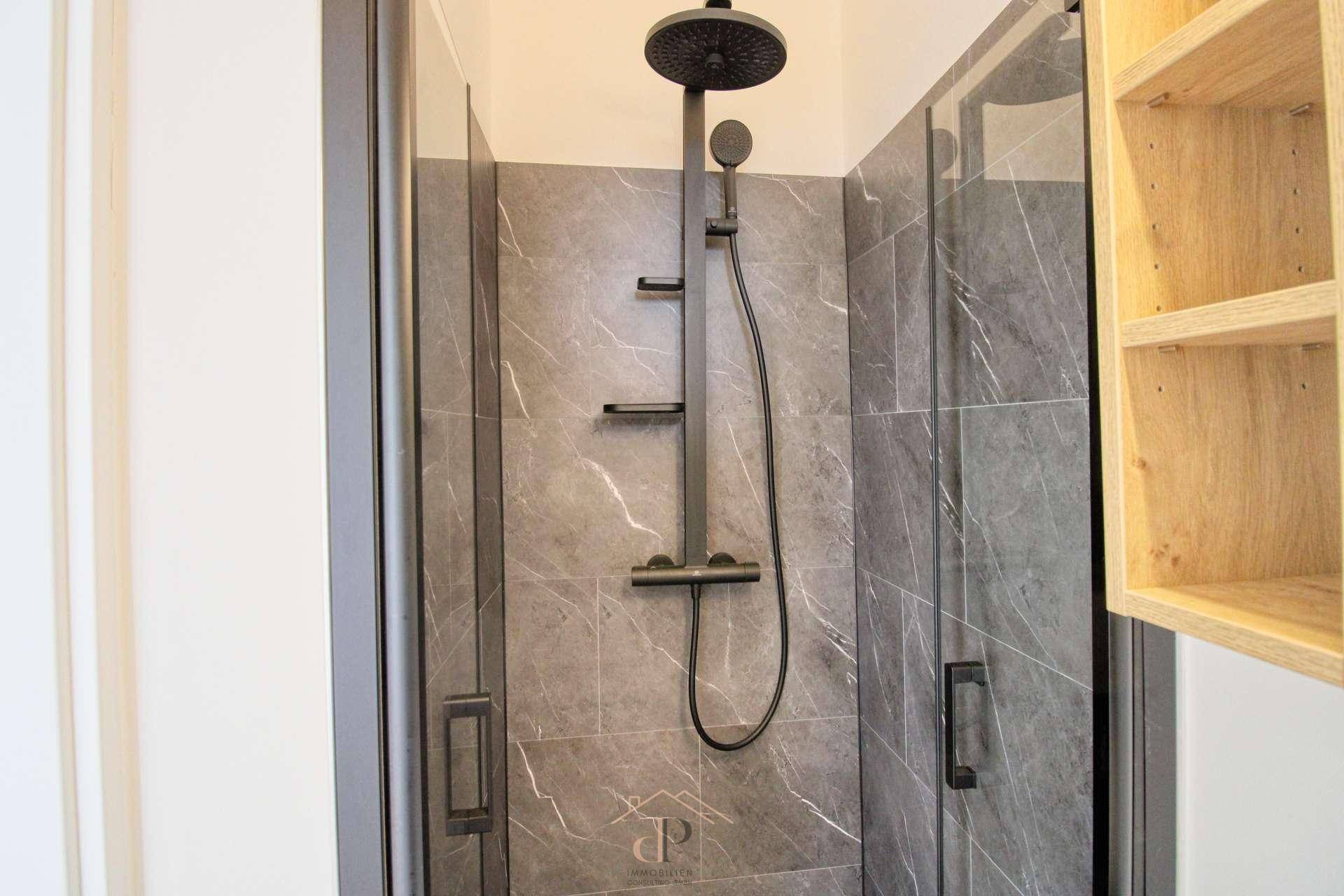 Detaillierte Ansicht der modernen Dusche mit Regenduschkopf und dunklen Marmoroptik-Fliesen.