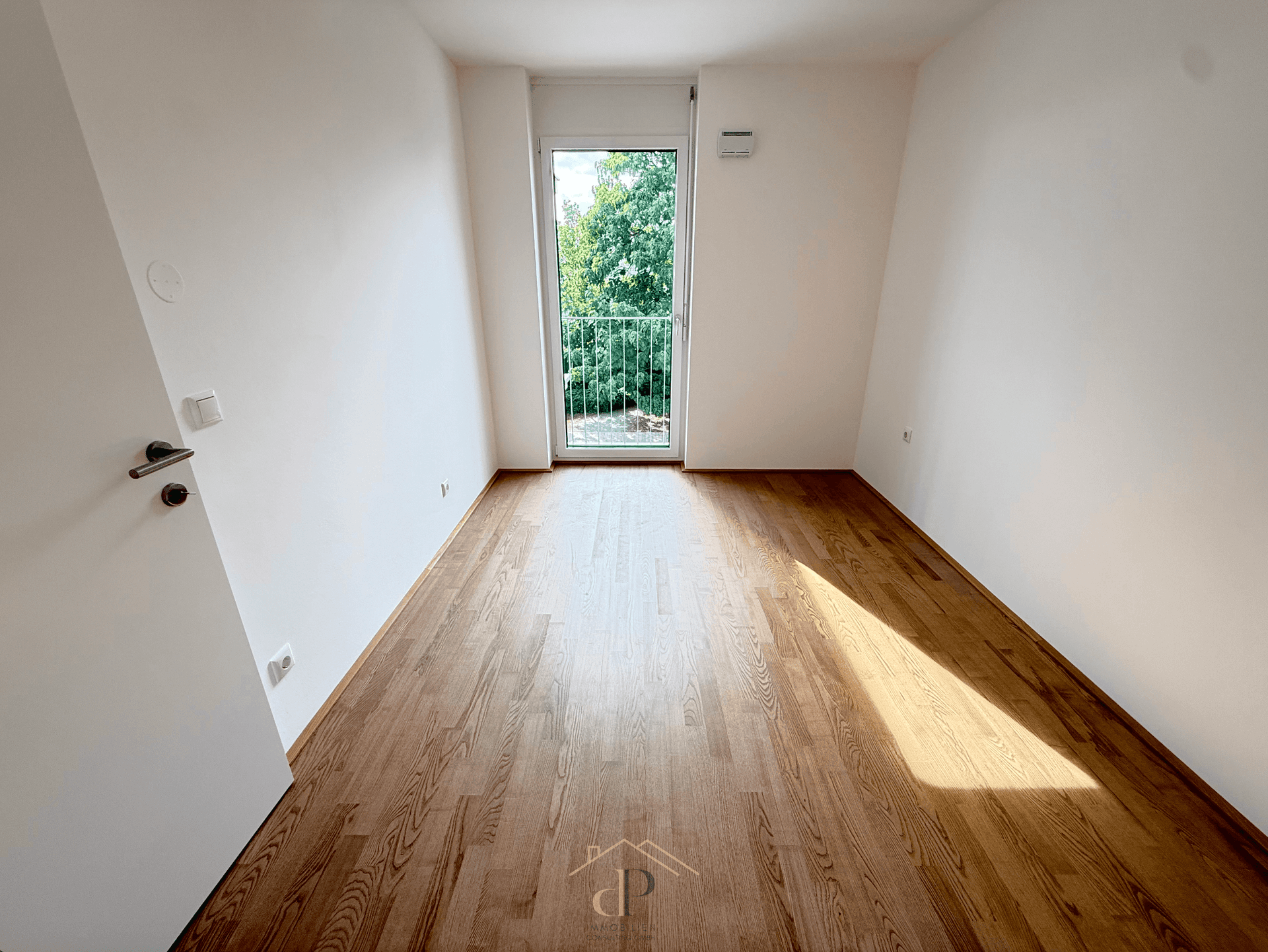 Helles Zimmer mit Parkettboden und Zugang zu einem französischen Balkon.