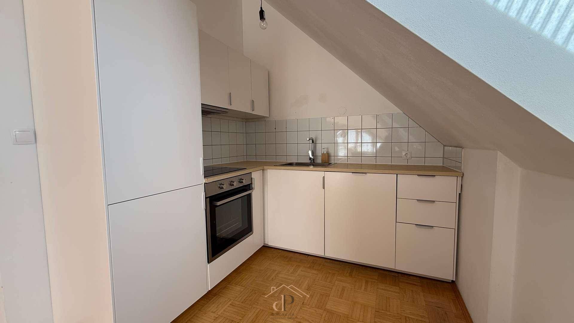 Funktionale Küchenzeile im Dachgeschoss mit weißen Schränken, Holzarbeitsplatte und Fliesenrückwand.