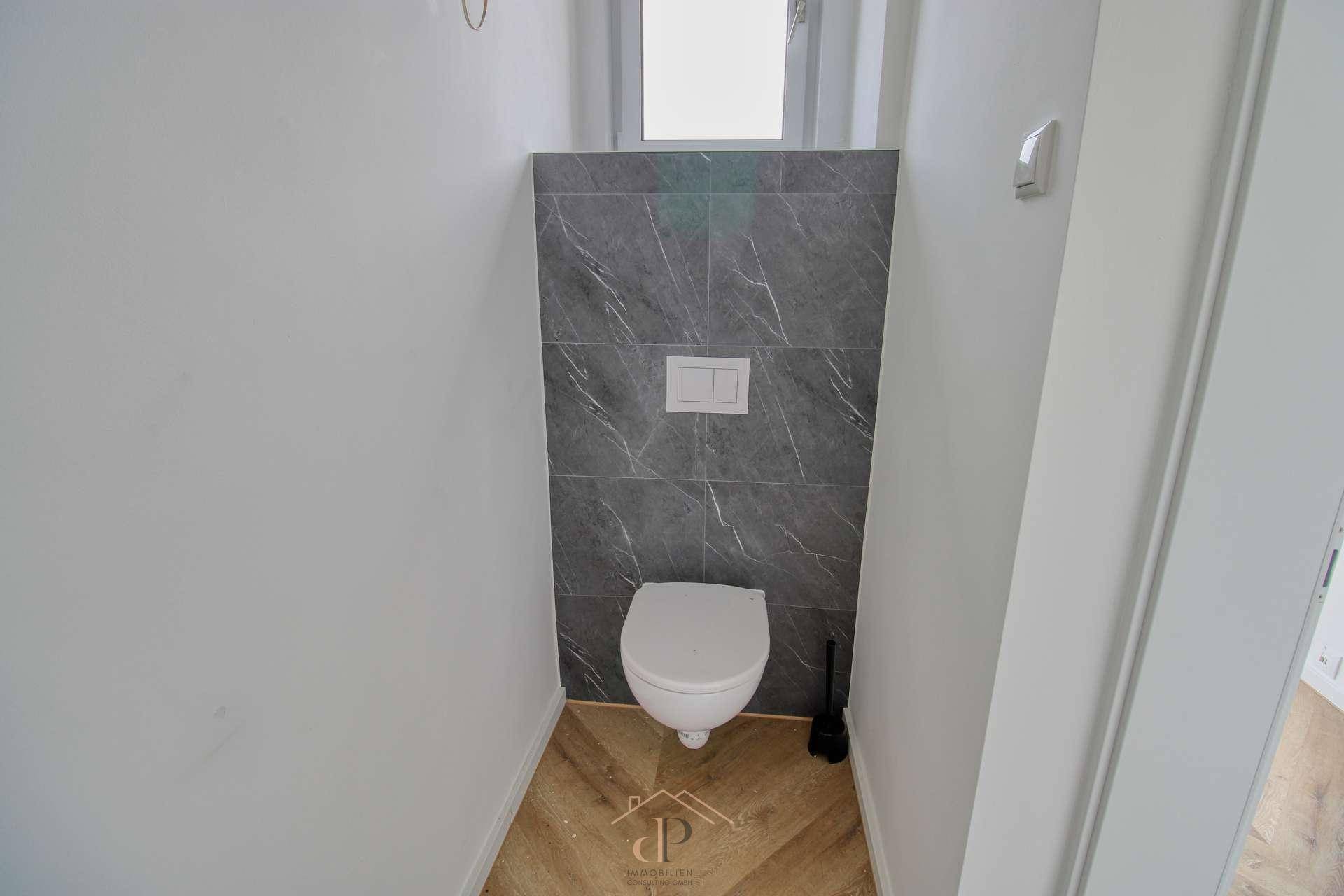 Modernes Gäste-WC mit wandhängender Toilette, dunklen Marmoroptik-Fliesen und Fenster.