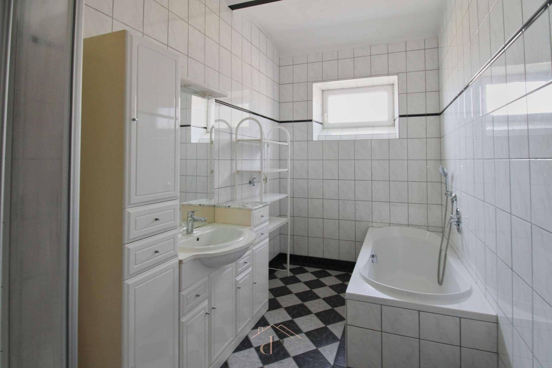 Badezimmer mit schwarz-weiß kariertem Fliesenboden, Badewanne und Waschtisch, hell und funktional.