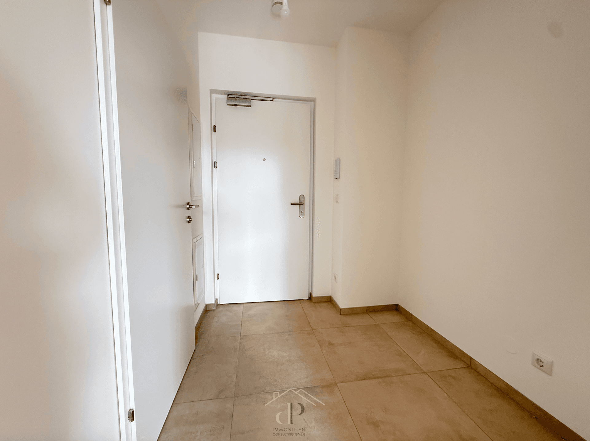Heller Eingangsbereich mit Fliesenboden und weißer Wohnungstür.