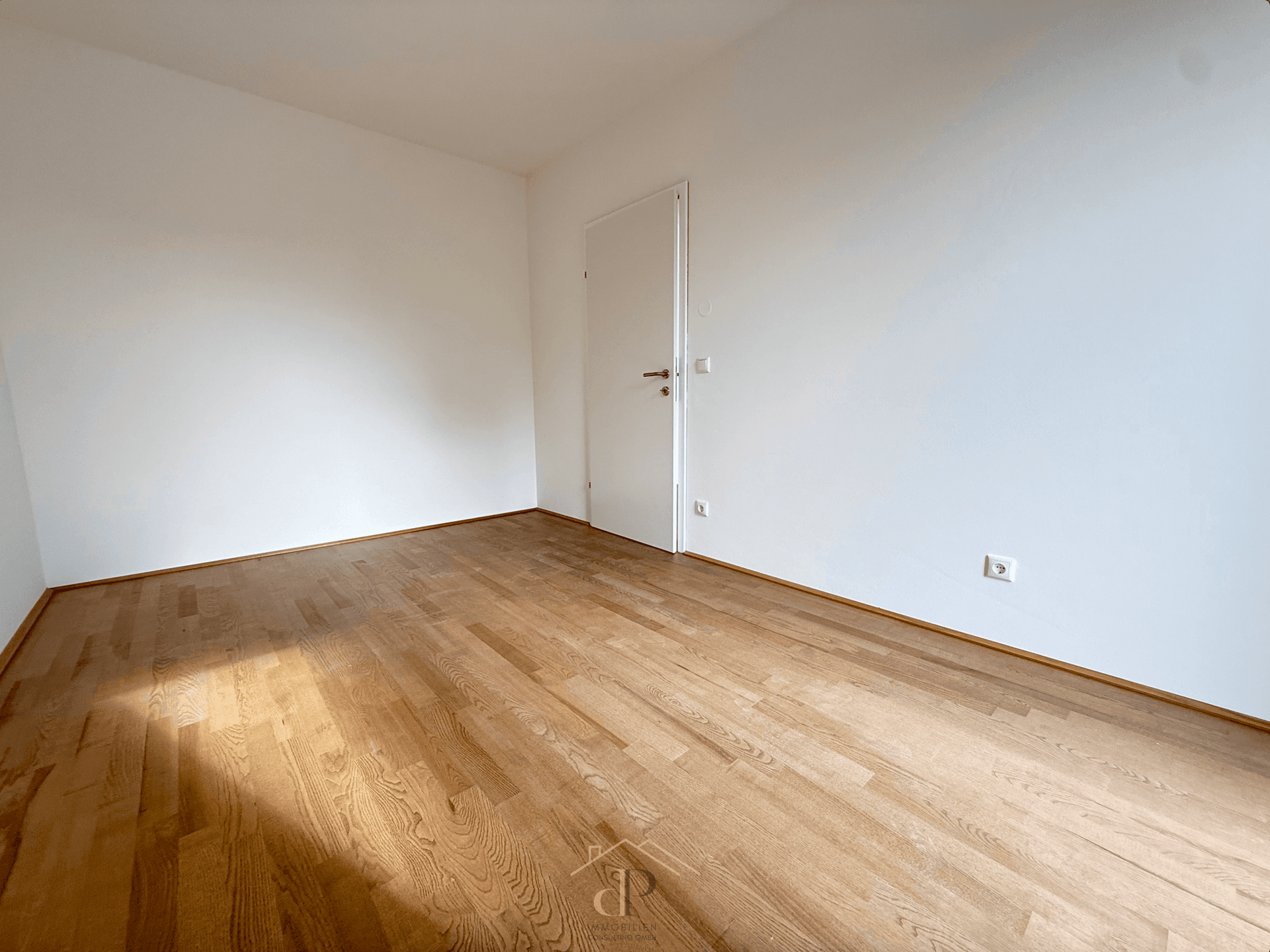 Leeres Zimmer mit Parkettboden und weiß gestrichenen Wänden.