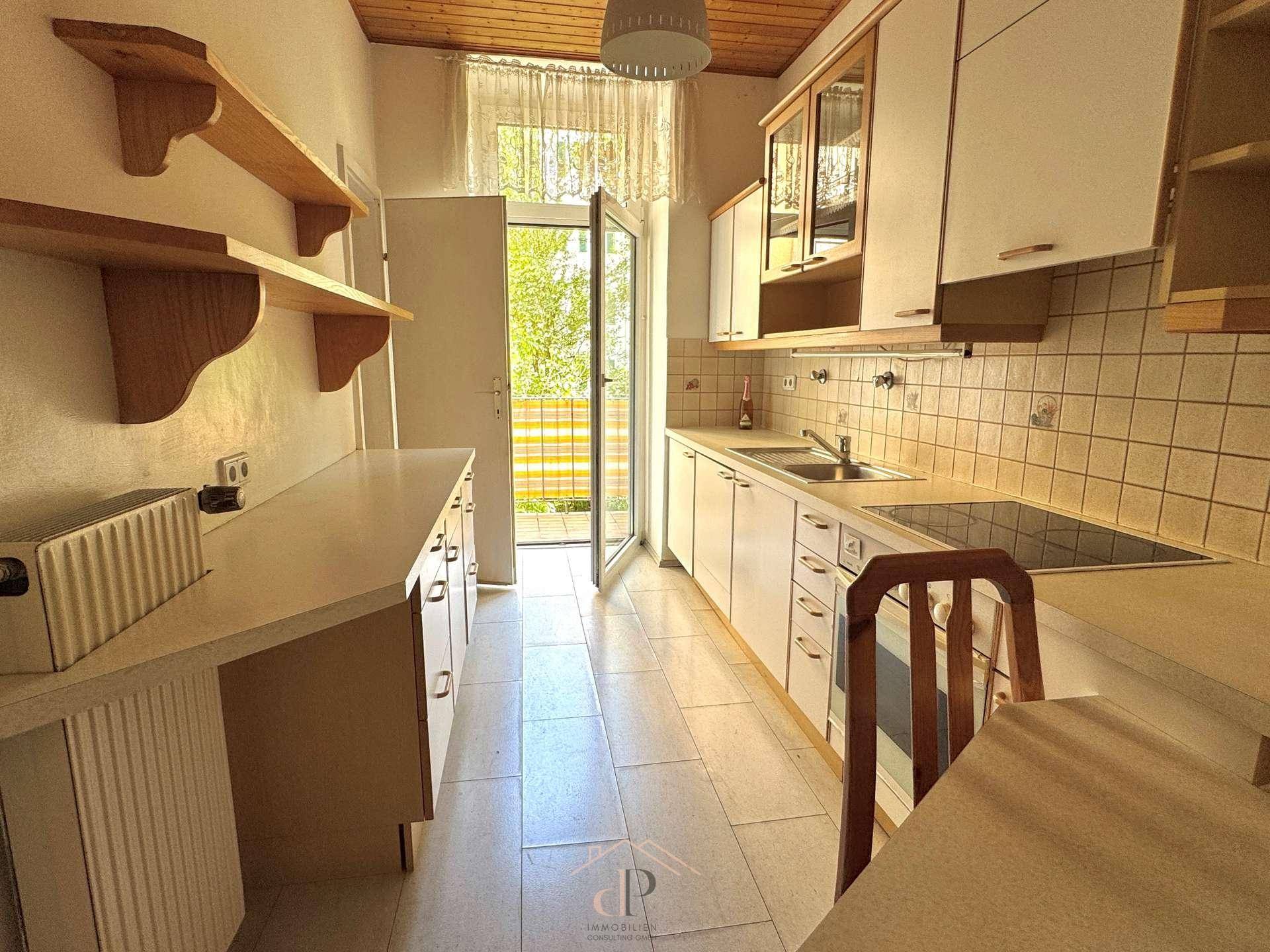 Funktionale Küche mit weißen Schränken, Fliesenboden und Zugang zum Balkon.