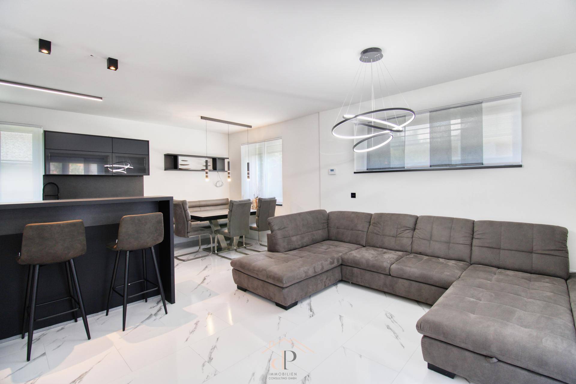 Offener Wohn- und Essbereich mit moderner Küche, großem Sofa und elegantem Marmorboden.