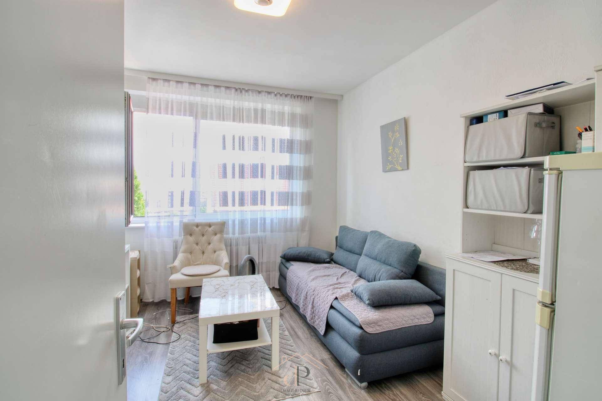 Kleiner Wohnbereich mit blauem Sofa, Couchtisch und einem großen Fenster für natürliches Licht.