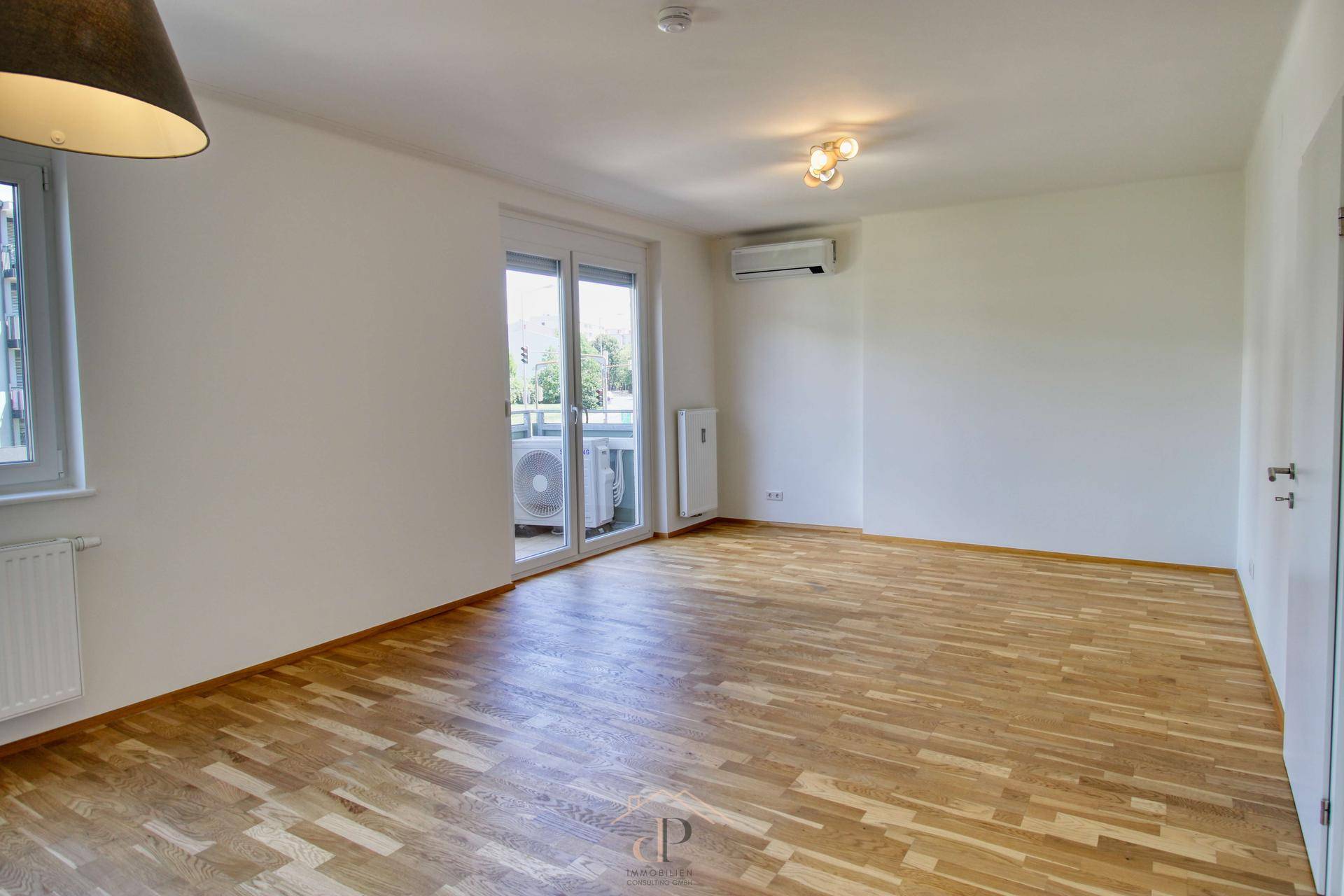 Geräumiges Wohnzimmer mit Holzboden, Klimaanlage und Balkonzugang.