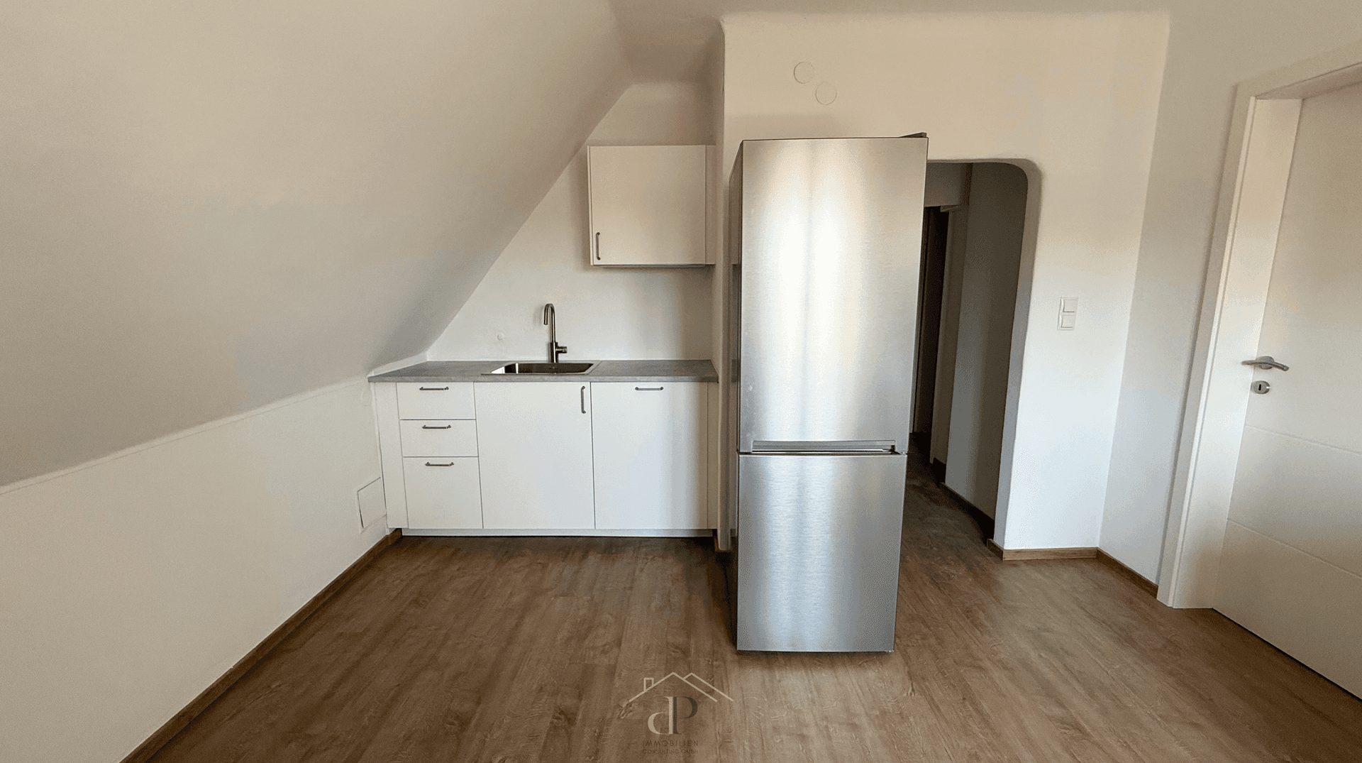 Kleine Küchenzeile im Dachgeschoss mit weißen Schränken und großem Kühlschrank.