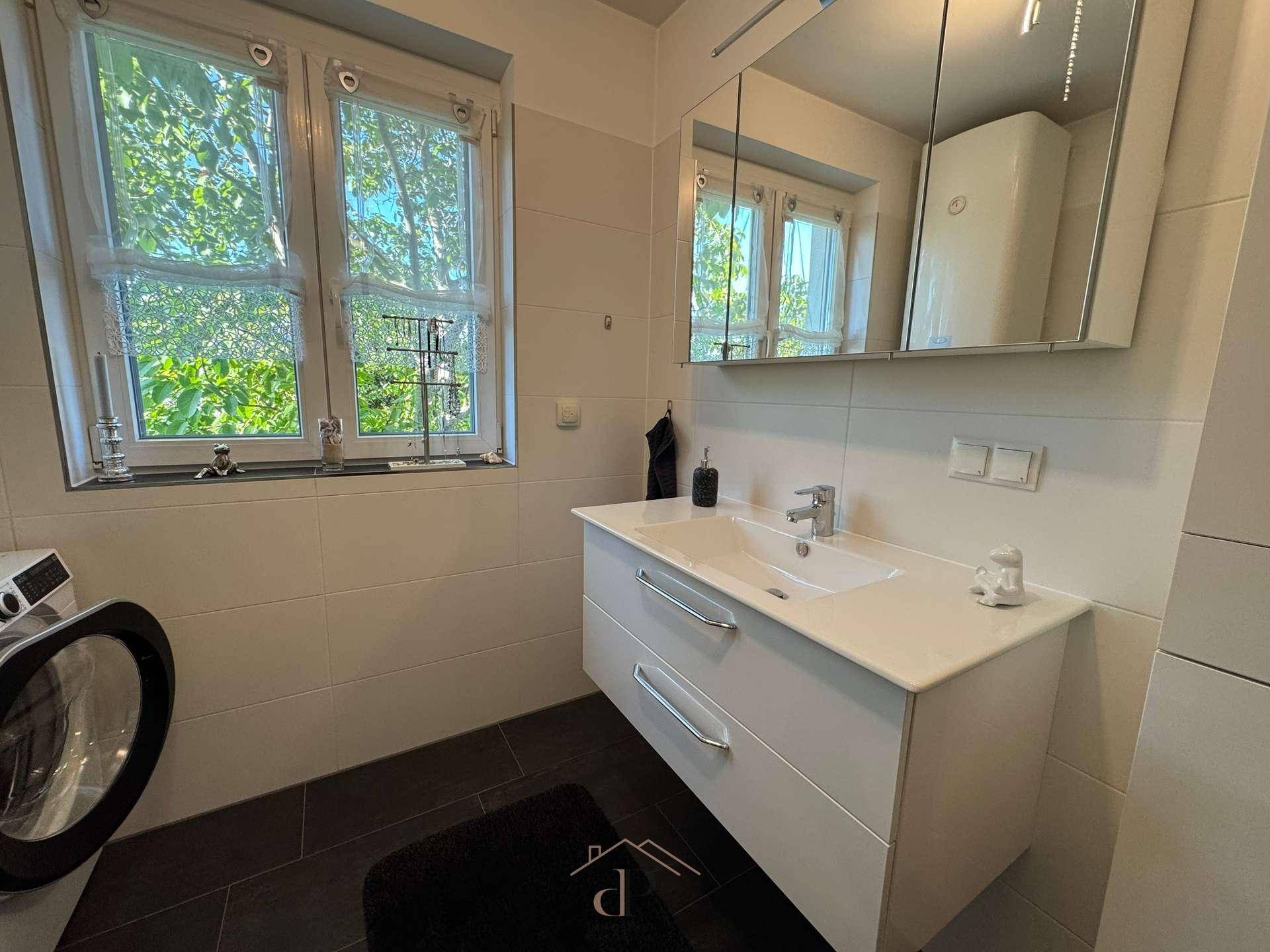 Helles Badezimmer mit modernem Waschtisch, Spiegelschrank und Fenster.