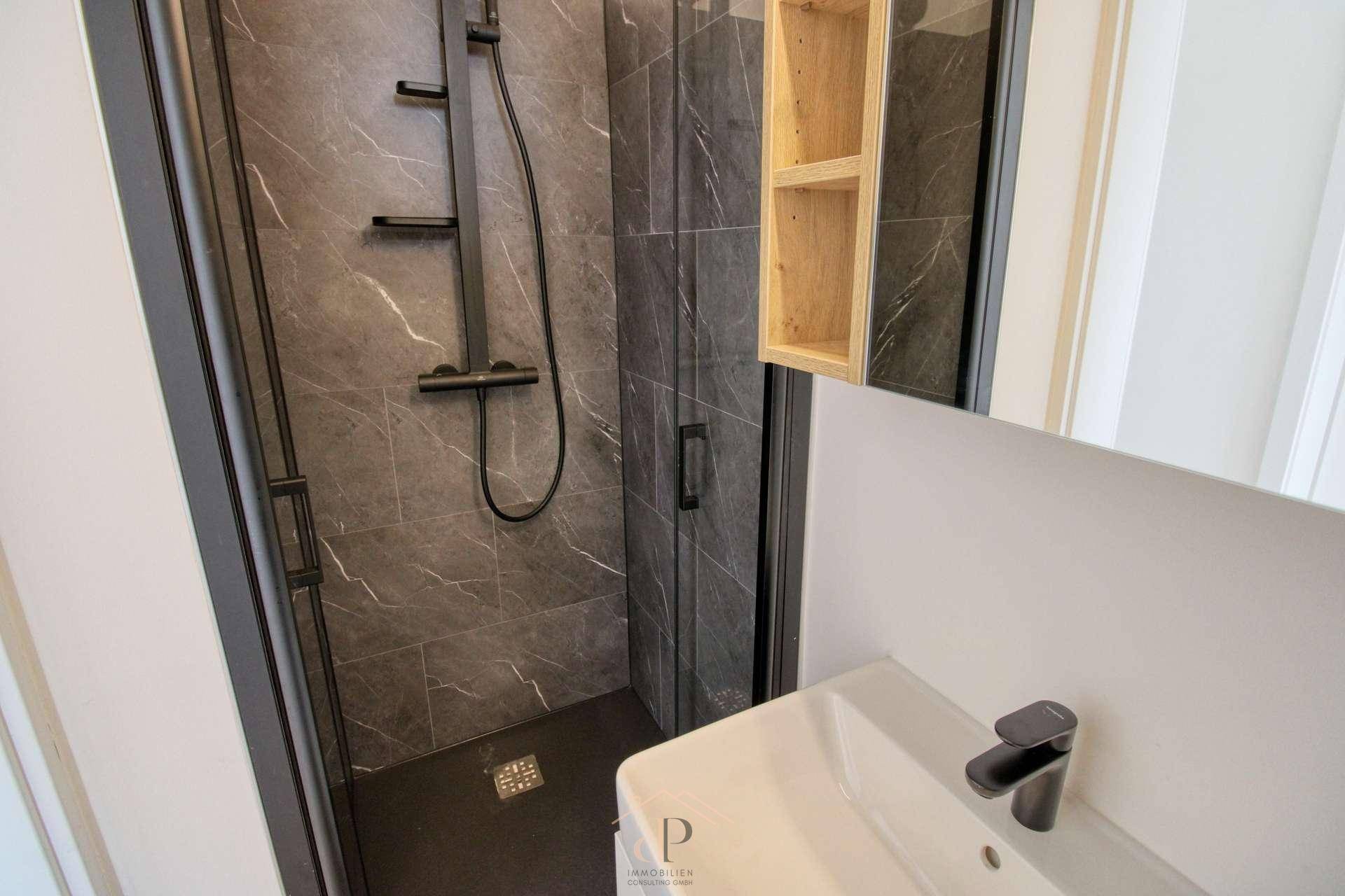 Modernes Badezimmer mit dunkler Duschkabine, Marmoroptik-Fliesen und eleganten schwarzen Armaturen.