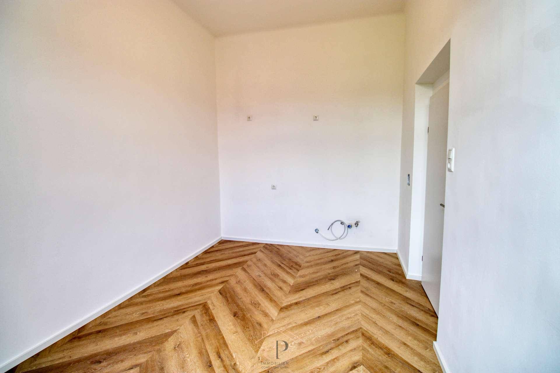 Leerer Küchenbereich mit Anschlüssen für eine Einbauküche und elegantem Fischgrätparkett.