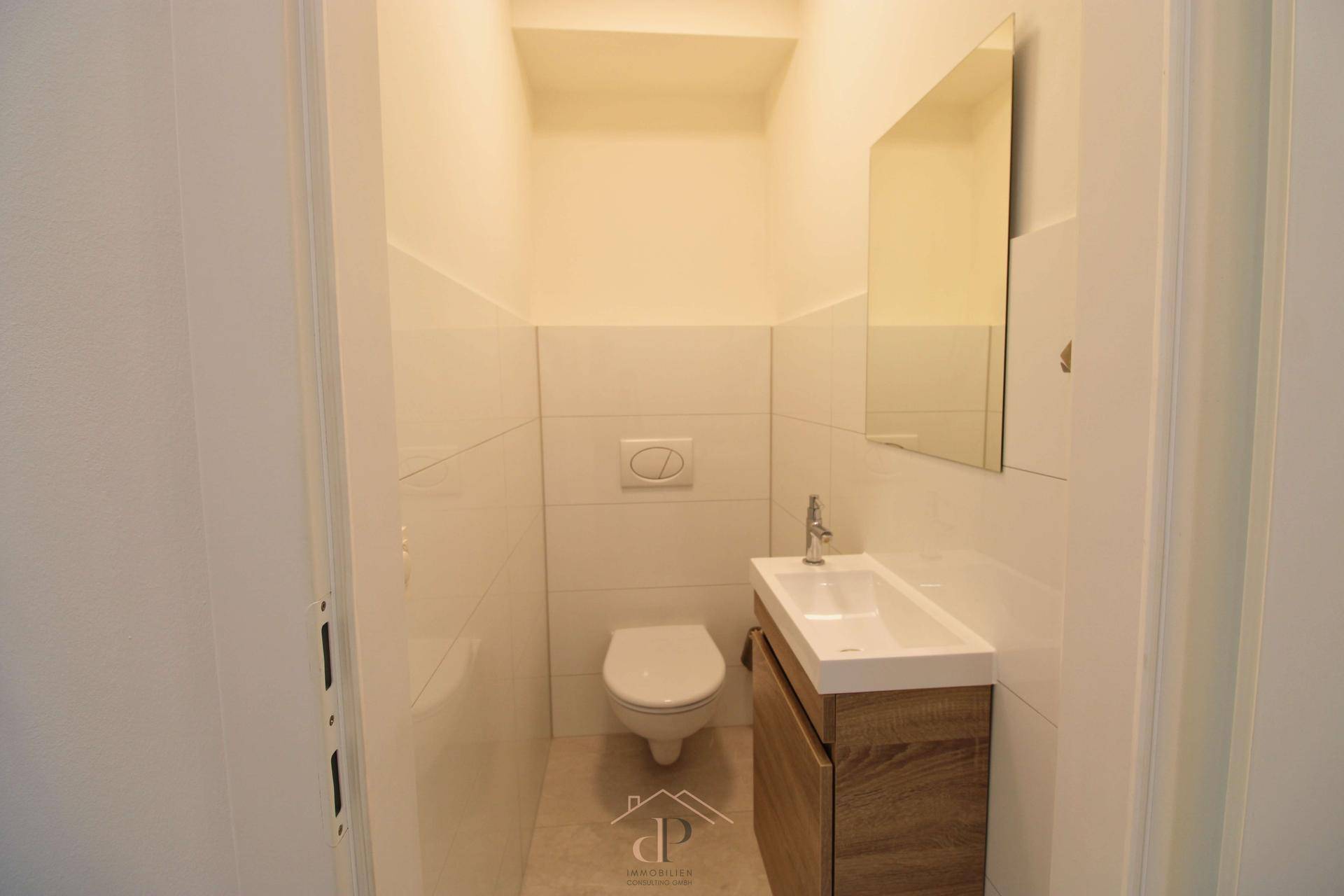 Modernes Gäste-WC mit wandhängender Toilette, kleinem Waschbecken und Spiegel.
