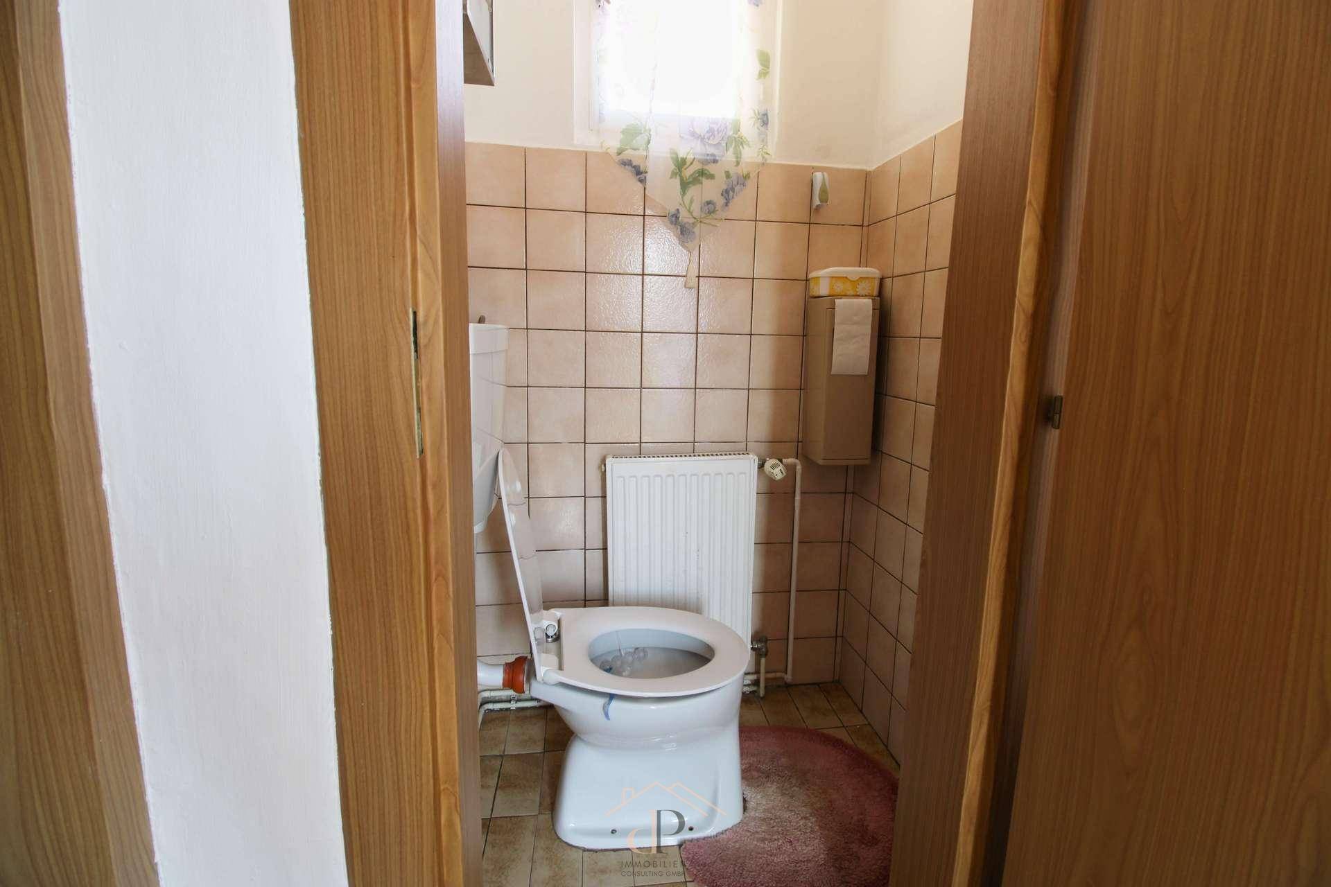 Kleines Gäste-WC mit beigen Fliesen und Fenster, funktional und hell.