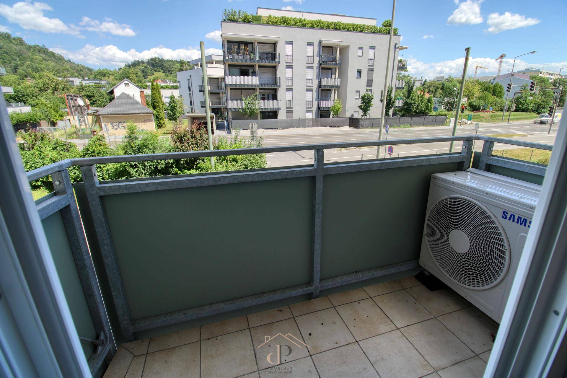 Balkon mit Klimaanlage-Außengerät und Blick auf die Straße und umliegende Gebäude.