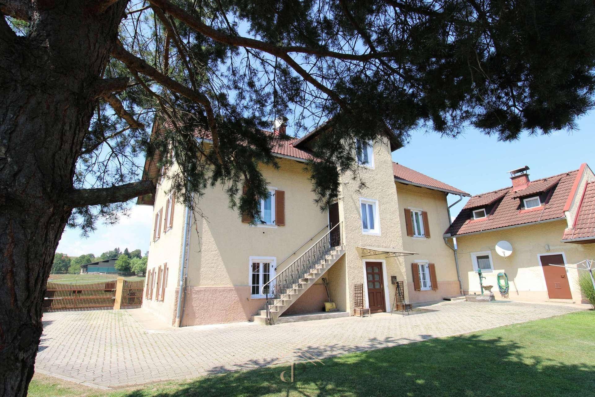 Charmantes Gebäude mit Außentreppe und gepflastertem Vorplatz, umgeben von grüner Landschaft.