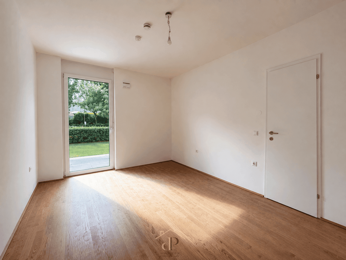 Leerer Raum mit Holzboden und direktem Zugang zu einem grünen Gartenbereich.