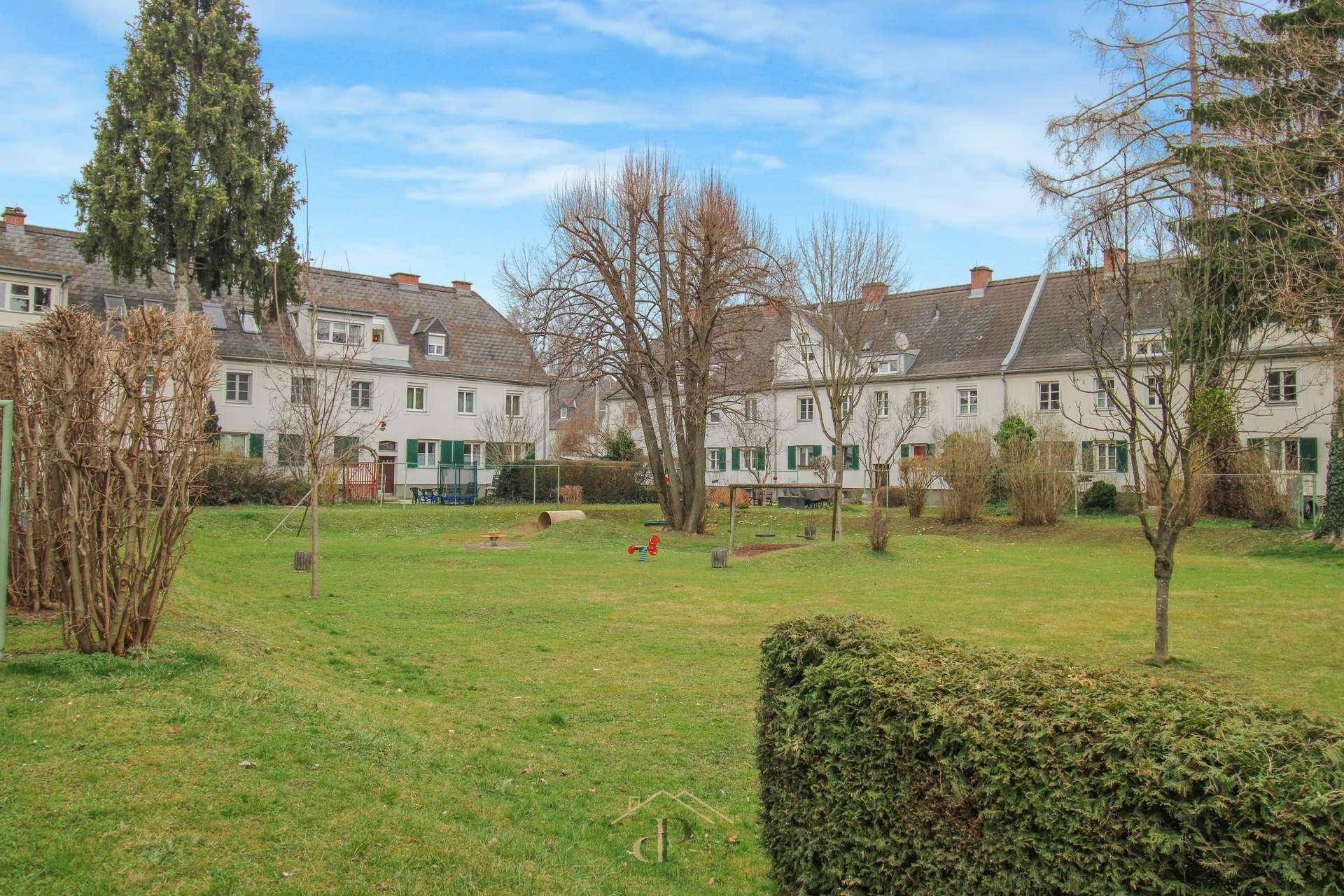 Grüner Innenhof mit Rasenflächen und Bäumen, umgeben von Wohngebäuden.