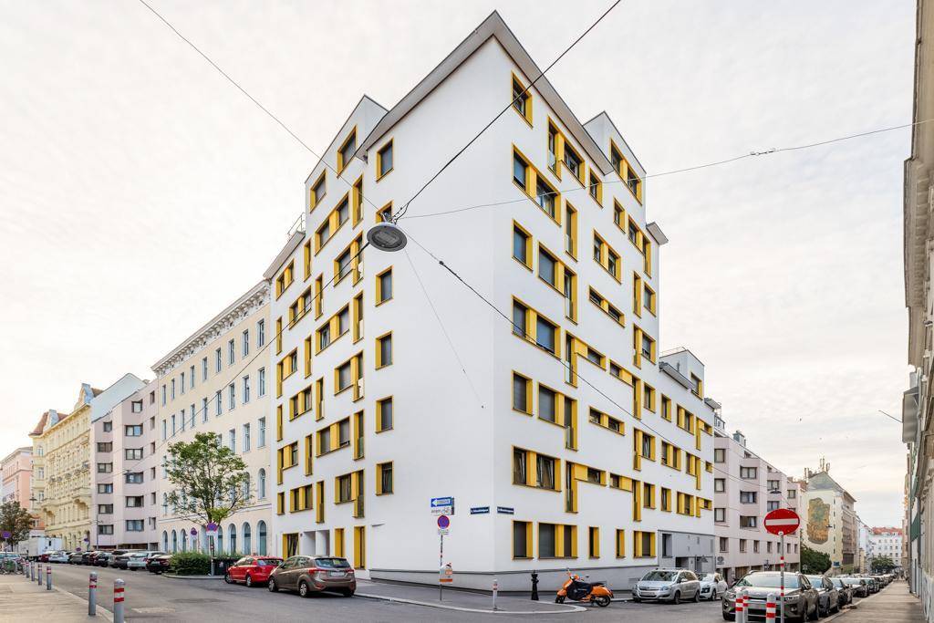 Modernes Gebäude mit weißer Fassade und auffälligen gelben Fensterrahmen in urbaner Umgebung.