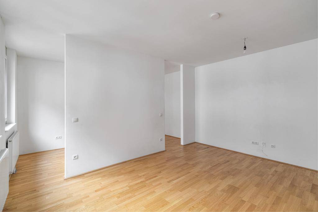 Geräumiger, heller Wohnbereich mit Holzboden und weiß gestrichenen Wänden, bereit zur Einrichtung.