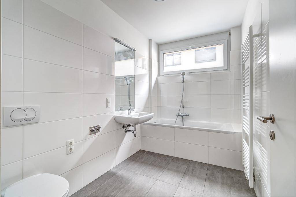 Modernes Badezimmer mit weißen Fliesen, Badewanne, WC, Waschbecken und beheiztem Handtuchhalter.