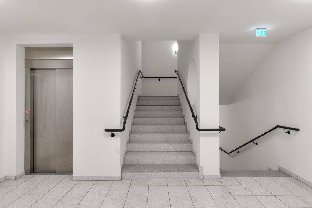 Treppenhaus mit Aufzug und Fliesenboden im Gemeinschaftsbereich des Gebäudes.