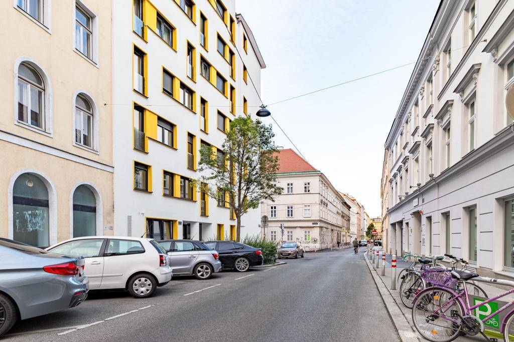 Ruhige Stadtstraße mit geparkten Autos und Fahrrädern, umgeben von Wohngebäuden.