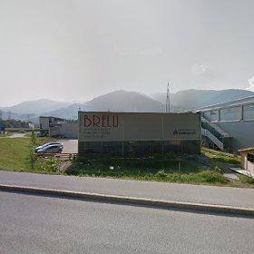 Geschäftsgebäude BRELU in einer ländlichen Umgebung mit Bergen im Hintergrund und einer Straße im Vordergrund.