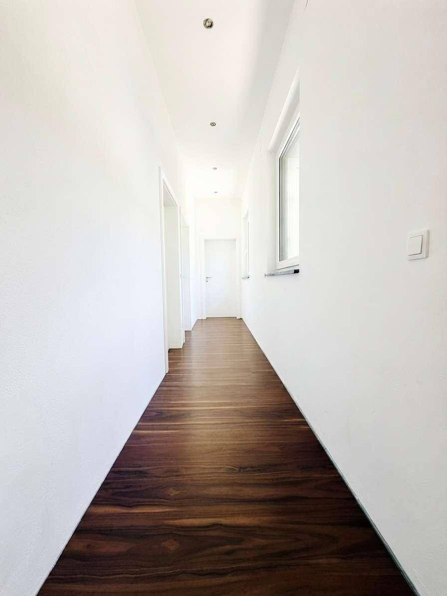 Langer, heller Flur mit dunklem Holzfußboden und weißen Wänden, ausgestattet mit Einbaustrahlern.