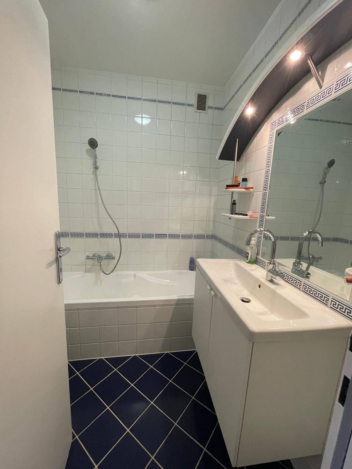 Badezimmer mit Badewanne, Einzelwaschbecken und weiß-blauen Fliesen.