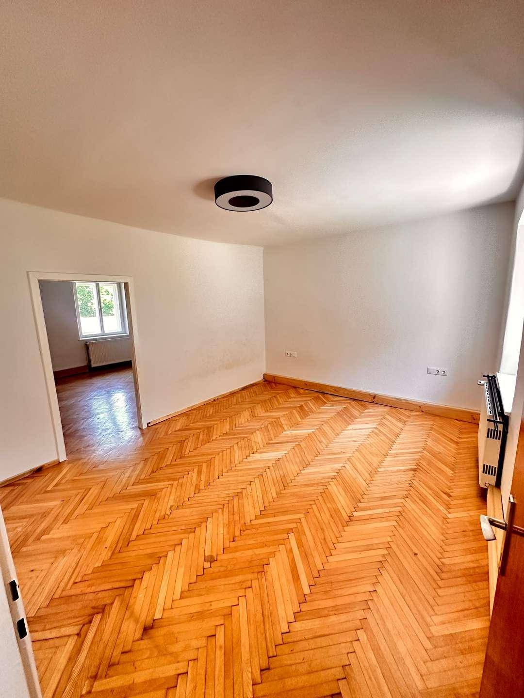 Großes Zimmer mit klassischem Fischgrätparkett und weißen Wänden, bietet viel Platz.