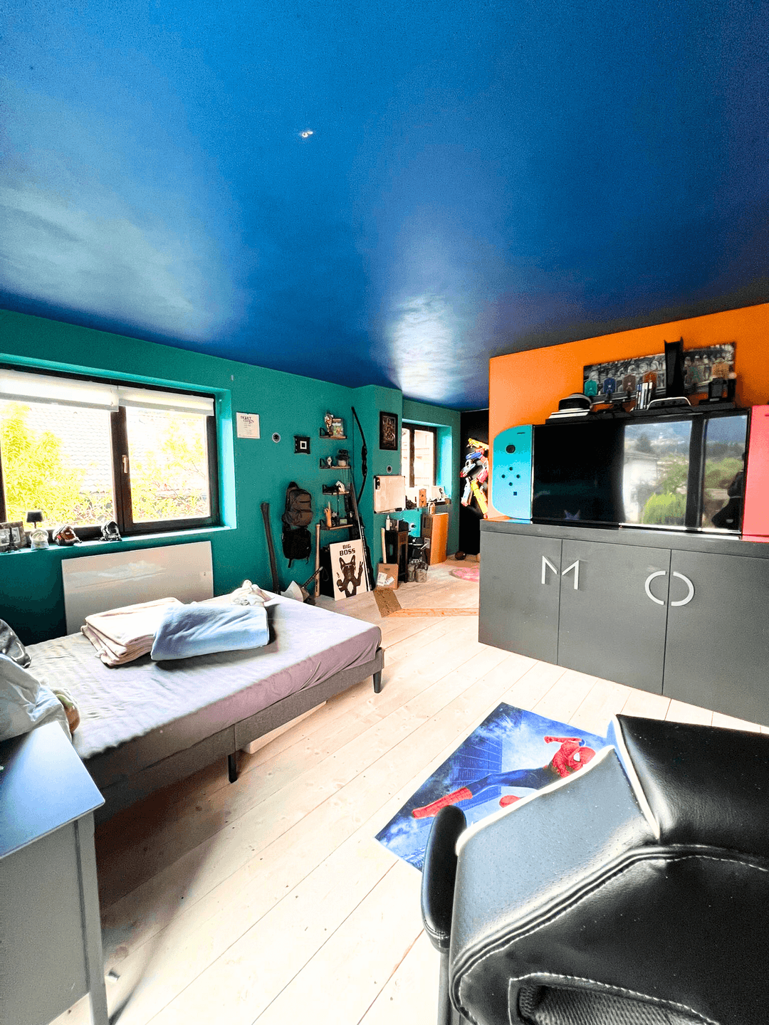 Farbenfrohes Schlafzimmer mit blau gestrichener Decke, grünen Wänden und hellem Holzboden.
