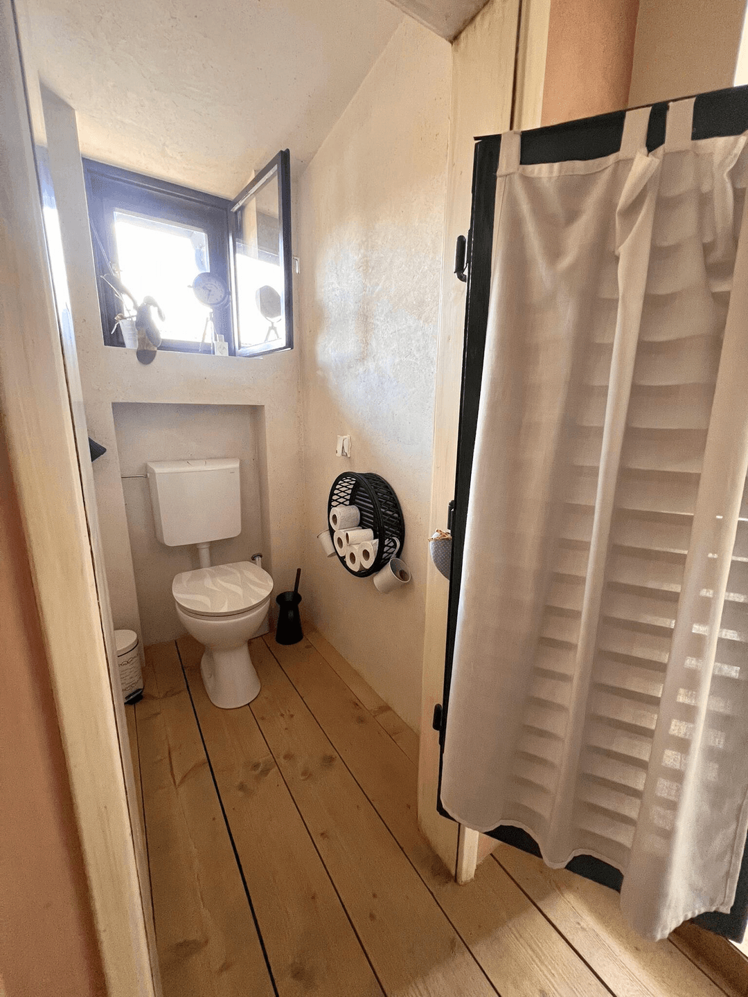 Kleines WC mit Holzdielenboden und einem Fenster für natürliche Belüftung.