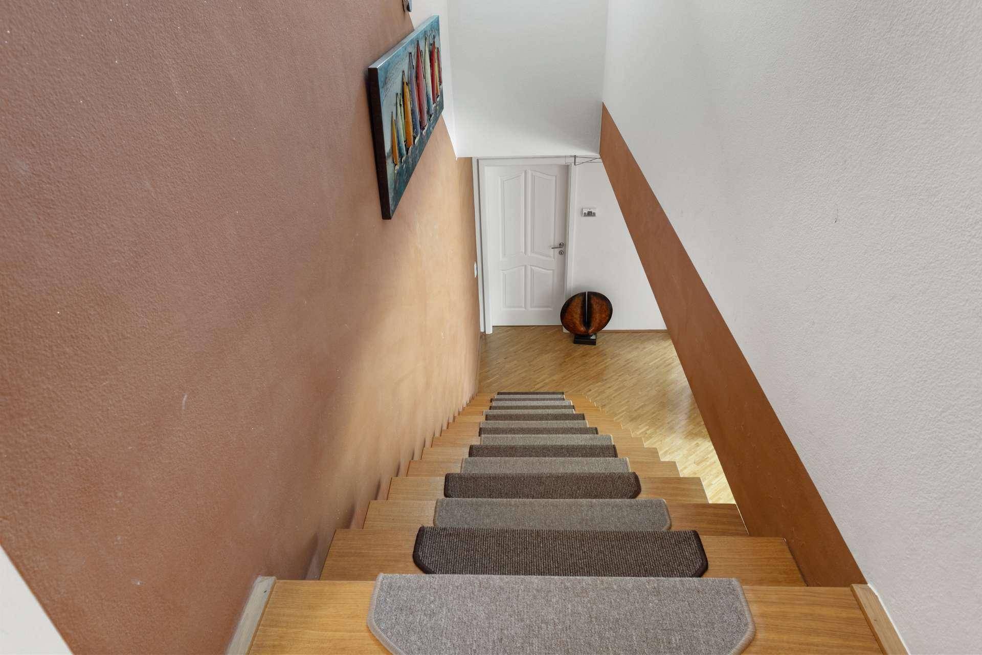 Treppenaufgang mit Holzstufen und Teppichläufern, der in das obere Stockwerk führt.