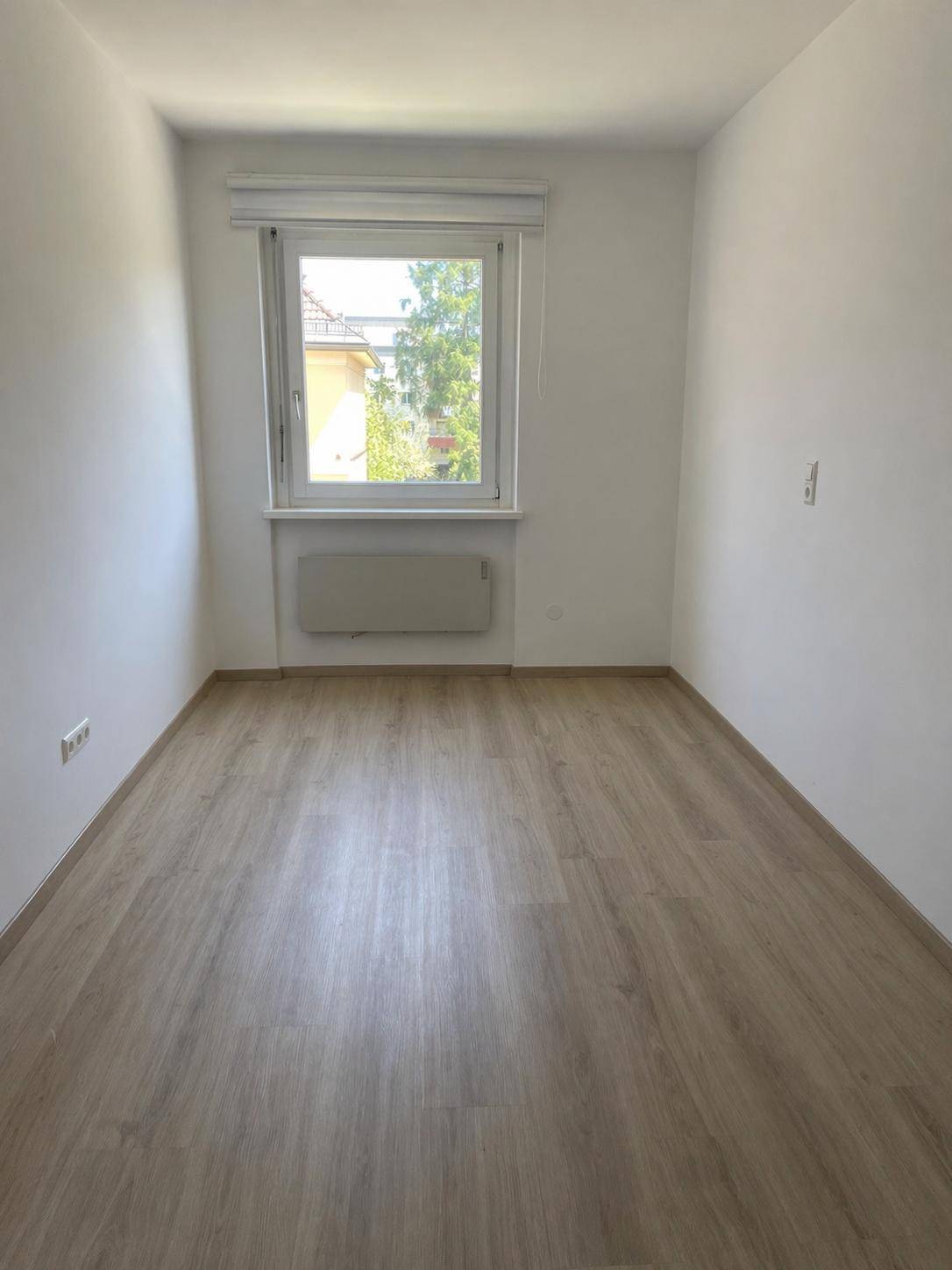 Helles Zimmer mit Laminatboden und großem Fenster, ideal als Schlaf- oder Arbeitszimmer.