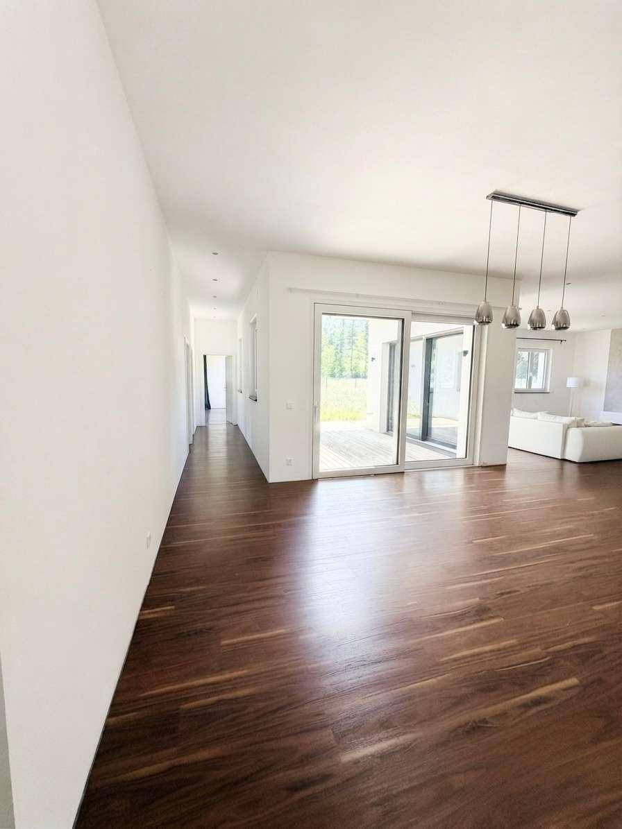 Offener Wohnbereich mit Holzboden, großen Schiebetüren zur Terrasse und moderner Beleuchtung.