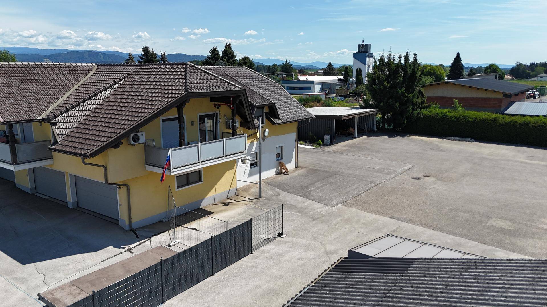 Wohnhaus mit mehreren Balkonen, Ziegeldach und großem gepflasterten Bereich im Vordergrund des Anwesens.