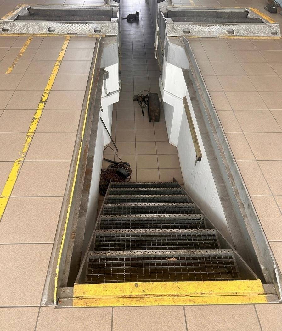 Detailansicht einer Inspektionsgrube mit Metalltreppe, die in den unteren Bereich der Werkstatt führt.