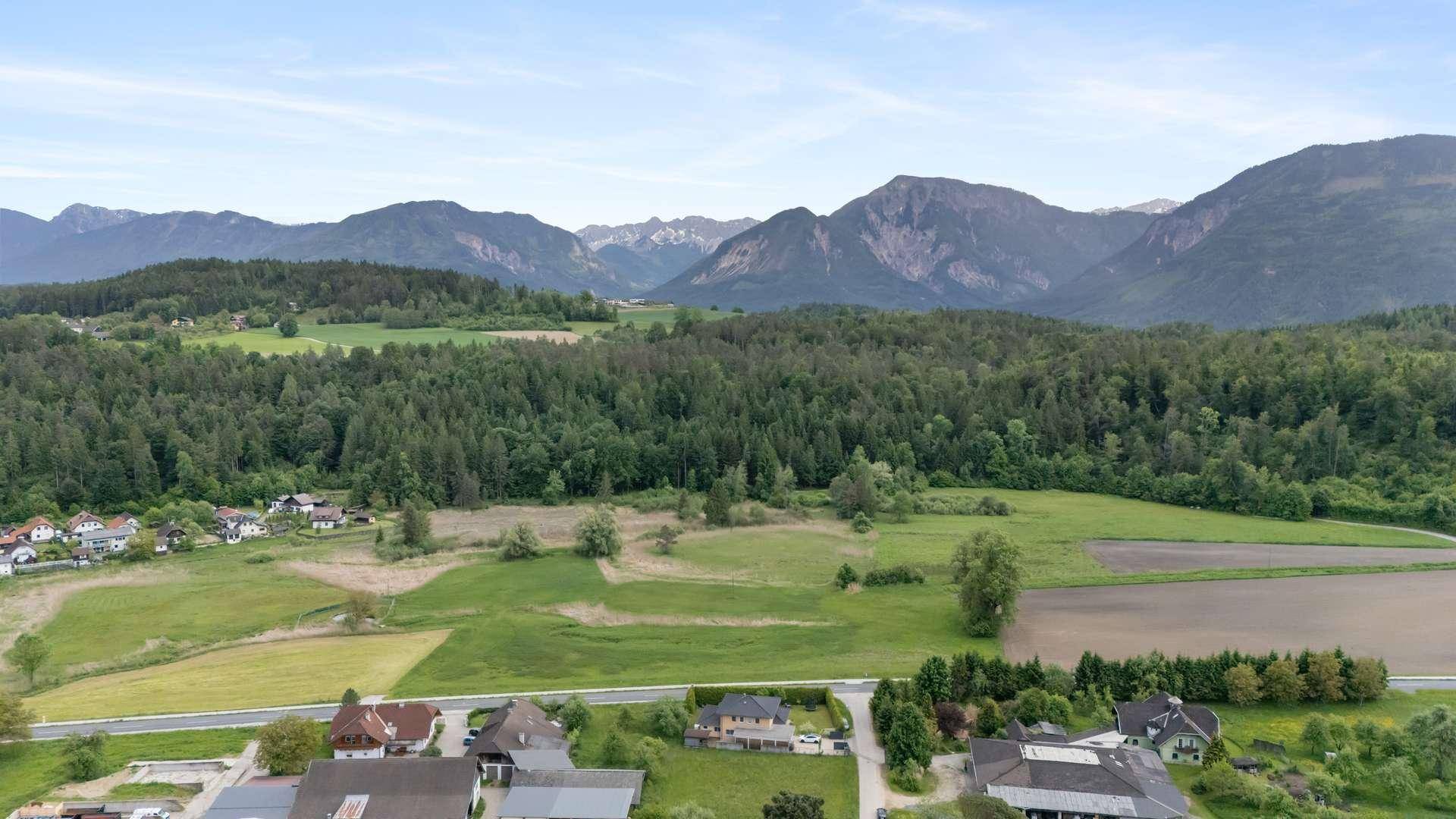 Panoramablick auf die ländliche Umgebung mit Häusern, Wäldern und majestätischen Bergen im Hintergrund.