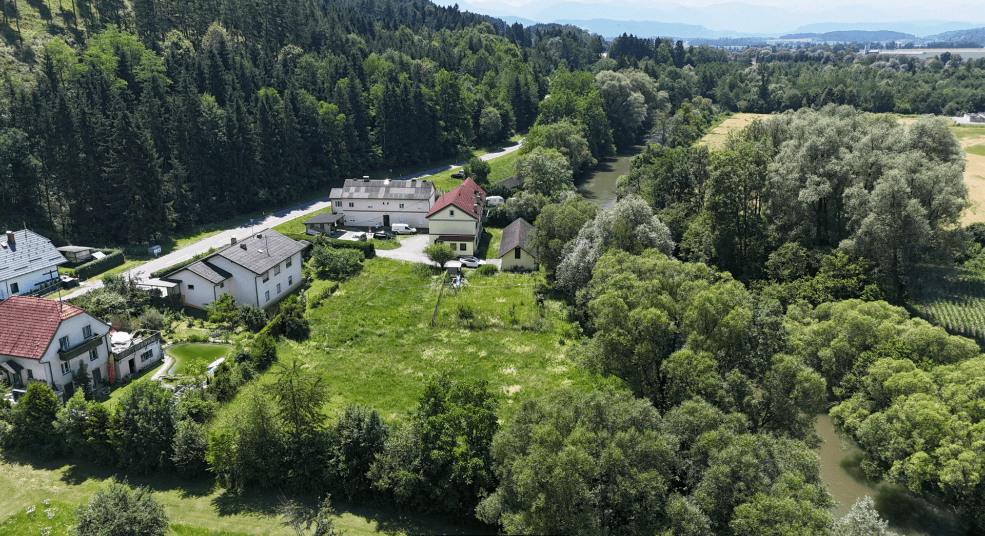 Luftaufnahme einer ländlichen Gegend mit Häusern, einem Fluss und üppiger grüner Vegetation unter blauem Himmel.