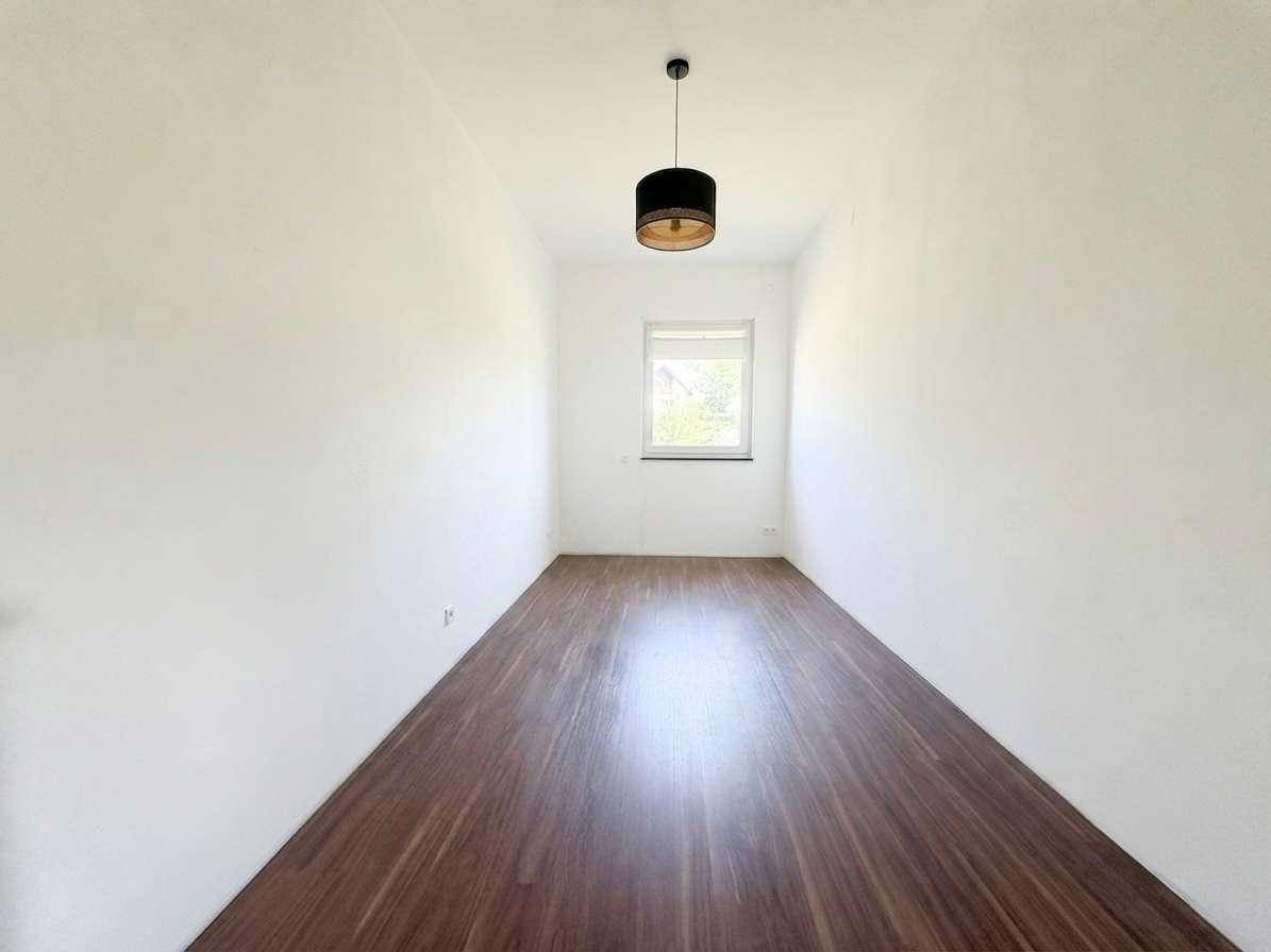 Schmaler, heller Raum mit Holzboden und einem Fenster, vielseitig nutzbar.
