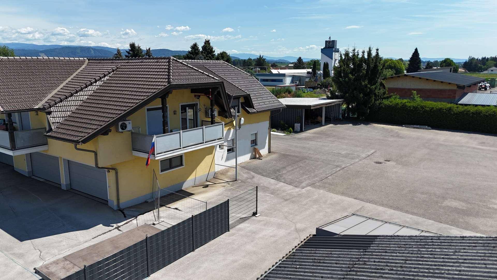 Wohngebäude mit mehreren Balkonen und Ziegeldach, umgeben von einer großen asphaltierten Fläche.