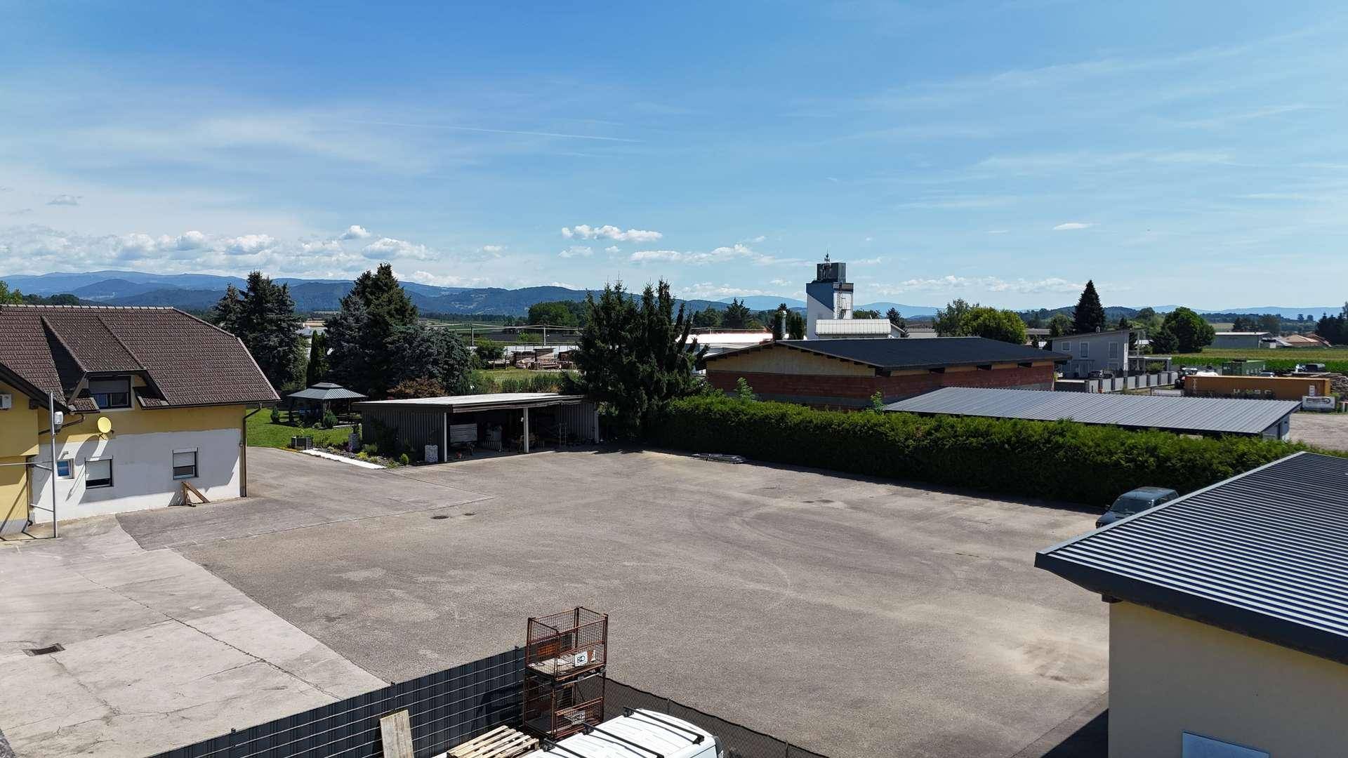 Großer asphaltierter Parkplatz vor einem Gebäude, umgeben von Bäumen und einer weiten Landschaft.