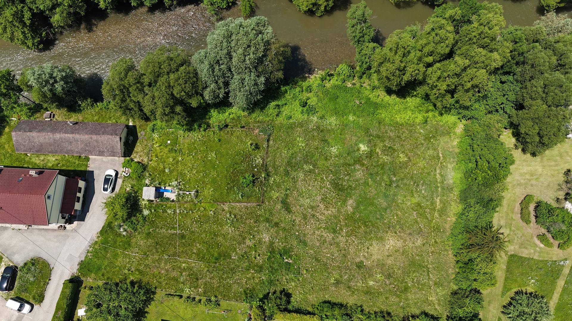 Luftaufnahme eines weitläufigen Grundstücks direkt am Fluss mit angrenzendem Gebäude.